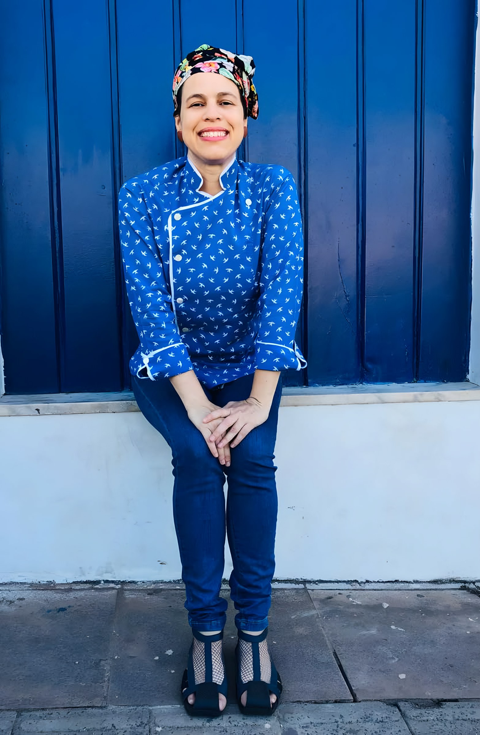 Maia Deva sentada diante de uma porta azul
