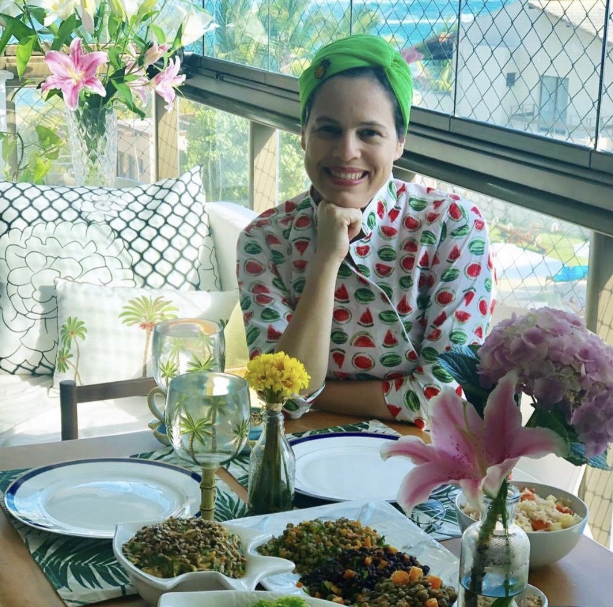 Maia Deva sorrindo à mesa com pratos naturais e flores